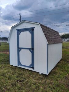a white barn style shed with blue trim and a brown roof in a open field